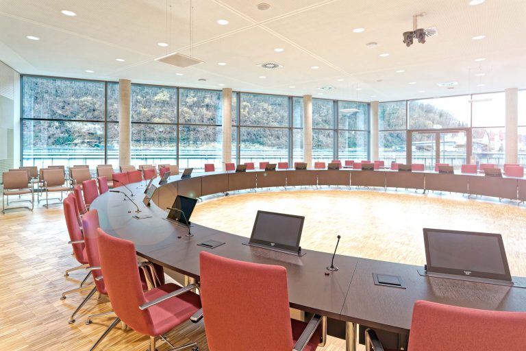 Moderner Sitzungssaal im Landratsamt Esslingen mit integrierter Konferenztechnik und ausfahrbaren Tischdisplays für digitale Gremienarbeit.